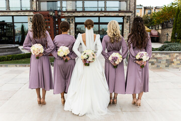 The bride and bridesmaids turned by their backs. Holding bouquets in their hands against the...