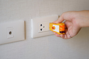 Hand holding electric tester for checking plug at the power outlet in on the wall. Check the...