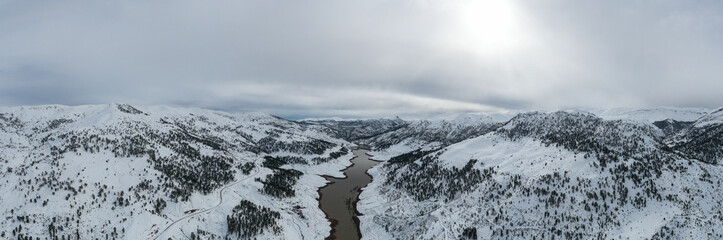 Aerial panoramic view of snow covered mountain and forest around beautiful lake. Scenic winter landscape near Haim, Konya, Turkey