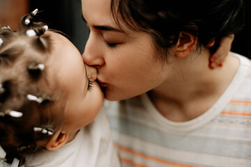 Mom hugs and kisses her daughter. Portrait of a child whose head is curled with homemade curlers