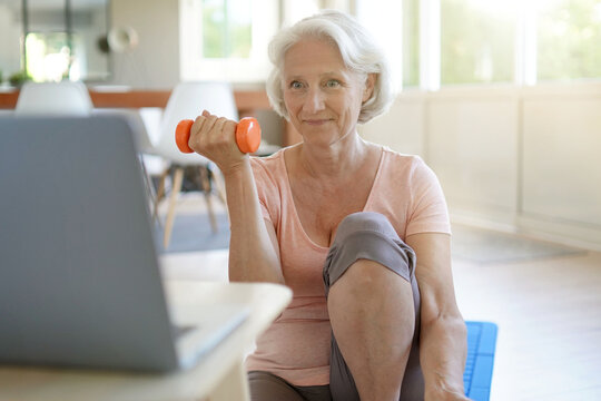 Senior Woman Doing Fitness Exercises At Home Through Virtual Class