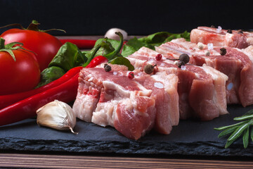 Raw slices of pork on a black slate board, tomatoes, red pepper and powder. Pork belly with vegetables.