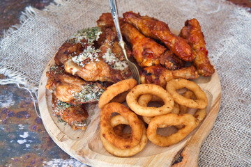 Delicious and unhealthy fast food - deep fried chicken wings with sweet chili sauce and parmesan with basil served with onion rings