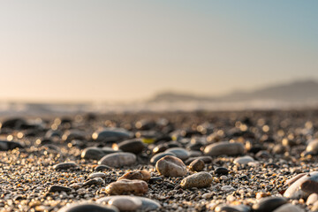 Close-up of pebble beach with light reflecting on stones against the blurred sky - Powered by Adobe