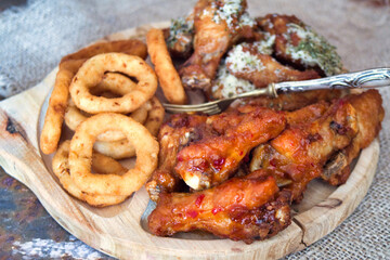 Delicious and unhealthy fast food - deep fried chicken wings with sweet chili sauce and parmesan with basil served with onion rings