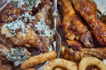 Delicious and unhealthy fast food - deep fried chicken wings with sweet chili sauce and parmesan with basil served with onion rings