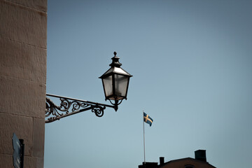 An old electric lamp mounted on a medieval building. The Swedish flag is visible in the background
