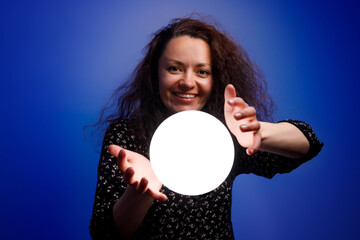 Smiling girl holding a glowing ball in her hands. Blue background.