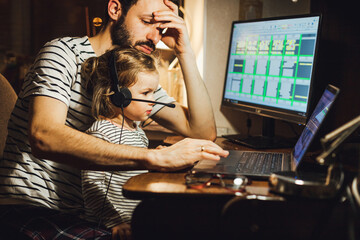 Stylish Bearded father working at home while babysitting his playful daughter