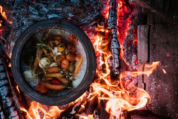 Cooking veggies on a camping trip on a fire with firewood top view. Cauldron on fire. Picnic....