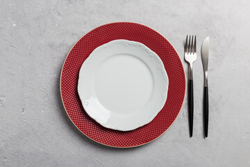 Minimal table setting with red and white dishes, fork and knife on gray concrete background