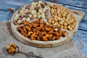 Variety of delicious nuts as heathy vegan appetizer - brazil nuts with chili, walnuts with garlic, sweet caramelized almond with cinnamon and macadamia on a rustic wooden board
