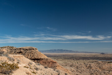 Distant mountains and desert plain seen from a rocky ridge, blue sky copy space, horizontal aspect