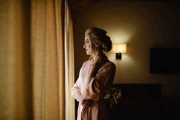 Beautiful blonde girl in a pink bathrobe looks out the window. Close-up.