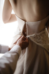 Gorgeous, blonde bride in a white luxurious dress getting ready for the wedding. Morning preparations. A woman puts on a dress. The groom helps the bride.