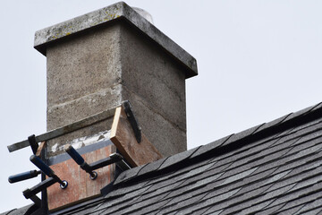Repaired chimney on grey asphalt shingles roof against sky with copy space for text.
