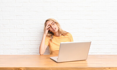 young blonde woman looking stressed, tired and frustrated, drying sweat off forehead, feeling...