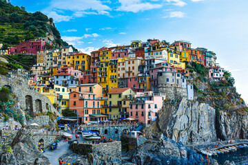 Fototapeta na wymiar MANAROLA - CINQUE TERRE, ITALY - August 24, 2019: View of the whole town of Manarola, UNESCO, on the shore with colorful houses on hot summer day