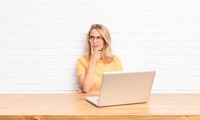 young blonde woman thinking, feeling doubtful and confused, with different options, wondering which...