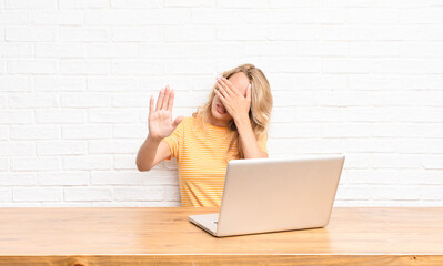 young blonde woman covering face with hand and putting other hand up front to stop camera, refusing...