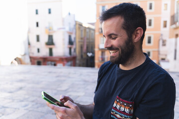 Image of a smiling young boy in a city square looking at his phone while chatting happily with friends.