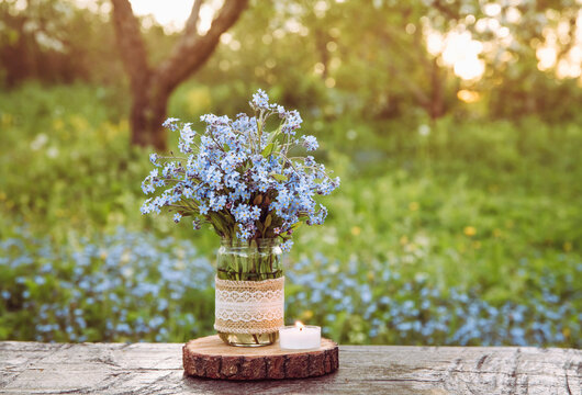 Bouquet of wild flowers Myosotis also known as Forget me not s or scorpion grasses in lace burlap cloth decorated baby food jar. Inexpensive vintage party decorations concept. Cozy spring evening.