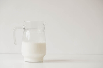 Glass jug with milk on a white table. Copy, empty space for text