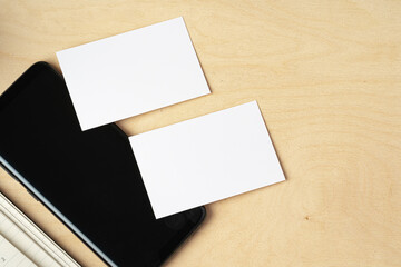 Fototapeta premium Mock up of blank business card and black smartphone screen on table