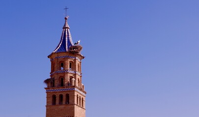Fototapeta na wymiar Dome of the catholic church made of red brick and decorated with blue and white ceramic tiles. Stork nests on top. Tauste, Zaragoza province, Aragon, Spain