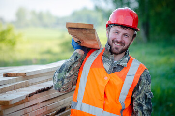 Builder in a protective helmet holds wooden planks. Concept - sale of lumber. Builder is considering wood planks. Concept - wood processing business. wood timber stack of wooden planks.