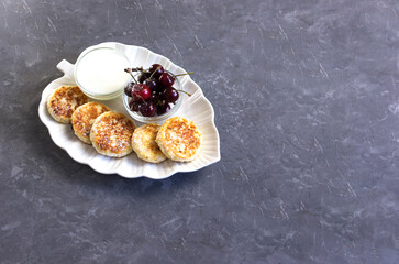 curd pancakes or cheese pancakes on a white plate in the form of a leaf with fresh cherries and sour cream, sprinkled with icing sugar, top view, copy space