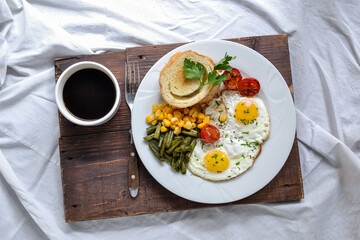 Breakfast in bed. Fried eggs with tomatoes, green beans, corn and toast. English vegetarian breakfast. Top view. Coffee and fried eggs on a wooden tray.