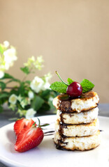 cheese pancakes or sirniki, stacked and decorated with mint and fresh cherries, vertical orientation, copy space, delicious breakfast