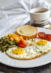 Breakfast in bed. Fried eggs with tomatoes, green beans, corn and toast. English vegetarian breakfast. Coffee and fried eggs on a wooden tray. Vertical view