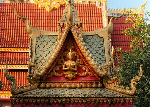 Colorful roof top religious architecture showing a praying buddha image at a temple site in Siamese Lao PDR, Southeast Asia