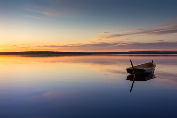 One small fishing boat on a pier by the lake during sunset. Long exposure photo