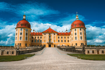 Fototapeta na wymiar Yellow Facade of Castle Moritzburg with orange roof, Saxony, Dresden, Germany. Beautiful spring day with blue sky and white clouds. Surrounded by beautiful park