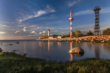 Shepelevsky lighthouse at the tip of the Karavaldai peninsula in the Leningrad region on a summer evening at sunset among a stone beach.