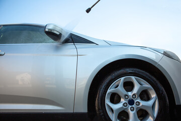 The gray car is washed under a strong stream of water. Car wash. Copy space.