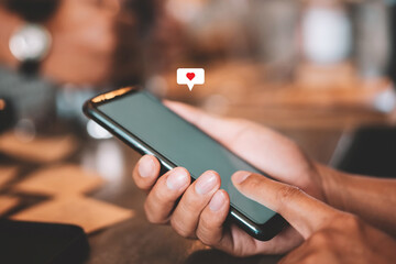 Man hand using smartphone with heart icon at coffee shop background. Technology business and social lifestyle concept.