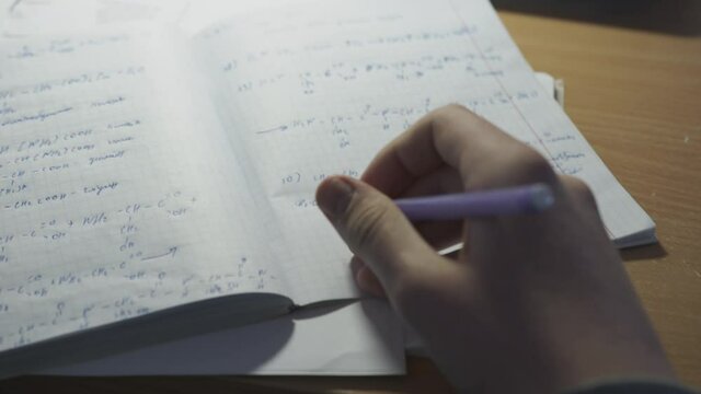 The man solves mathematical problems in a notebook and prepares for training. Man writes with a pen formula in a notebook close up.