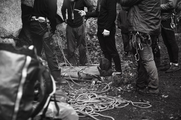 Group of rock climbers and the body of the injured laid on a stretcher for transportation, during rescue operation, black and white.