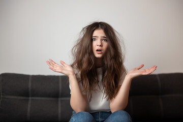 brunette young woman with tangled long hair looks desparate and unhappy with her hairstyle, bad...