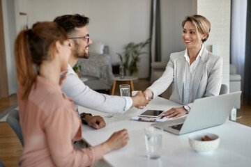 Happy real estate agent shaking hands with a couple on a meeting in the office.