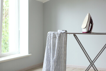 Iron and ironing board in a bright room. Iron clothes.
