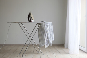 Iron and ironing board in a bright room. Iron clothes.
