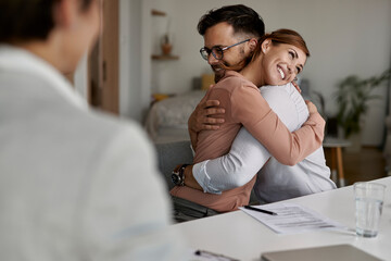 Happy couple embracing after signing a contract with real estate agent.