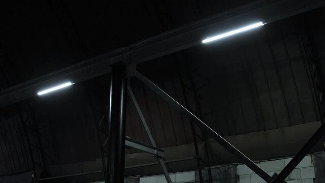 Led lights lamps on metal beams partitions blink and turn on in dark room of plant without windows, hangar, workshop department. Power failure, network electrical short circuit in industrial area