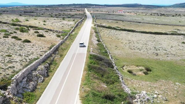 Scenic road on the island of Pag in Croatia, car drive between old agriculture fields and stone drywals
