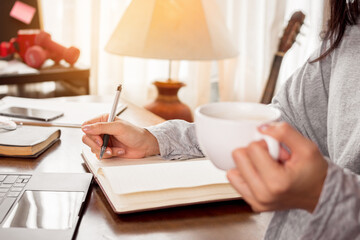 Close up woman hand is writing note for work and drink coffee at home.
